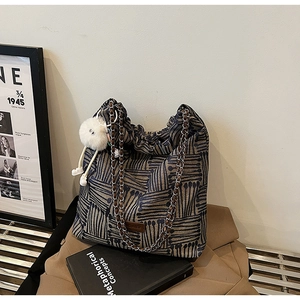 Detail of canvas bucket bag with blue geometric lines, chain strap and plush pendant