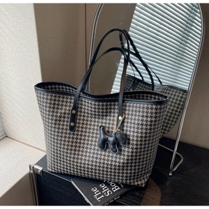 Detail of houndstooth tote bag with black leather trim and puppy charm on black surface