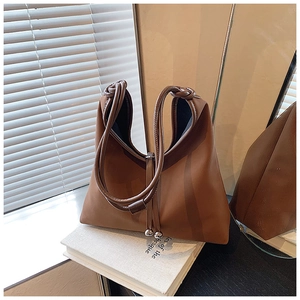 Detail of caramel leather tote bag featuring knotted handle and silver metallic ball charms