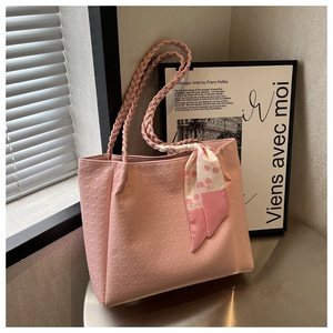 Detail of light pink tote bag with woven handles and cherry print silk scarf on metal surface