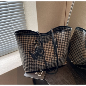 Detail of houndstooth tote bag with slim black shoulder straps and a dog shaped charm