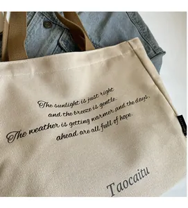 Detail of canvas tote bag showing thick beige fabric, brown straps and printed text