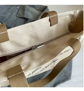 Detailed macro view of the silver metal zipper closure on the off-white canvas tote bag