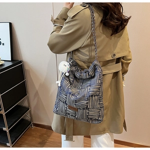 Detail of canvas striped tote bag with silver chain strap and plush ball charm accessory