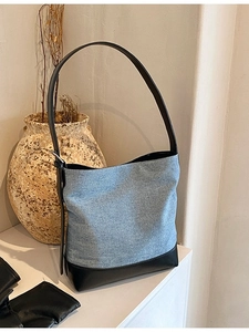Large capacity denim and black leather bucket bag with shoulder strap in a rustic setting