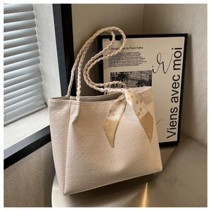 Detail of cream tote bag with houndstooth texture, braided handles and silk scarf