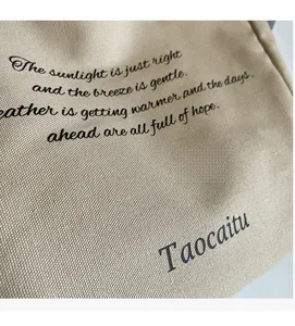 Detail view of beige canvas tote bag showing textile texture and artistic typography print