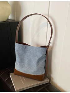 Retro denim and caramel leather bucket bag on vintage books in a soft indoor setting