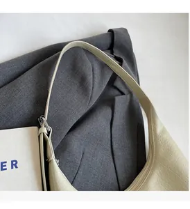 Detail der beigen Leder-Beuteltasche mit Silberschnalle auf grauem Blazer-Hintergrund
