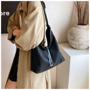 Detail of a large black tote bag with drawstring and metallic sphere on a trench coat