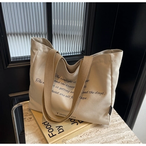 Detail of beige canvas tote bag with woven handles placed on books in a cozy setting