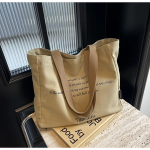 Close-up of beige canvas tote bag with black artistic print and brown woven handles