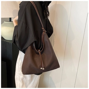 Detail of dark brown tote bag featuring knot shoulder strap and silver ball drawstring close