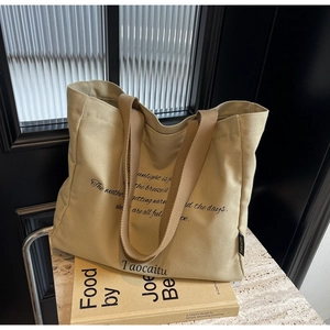 Detail of khaki canvas tote bag with brown straps and artistic black text branding
