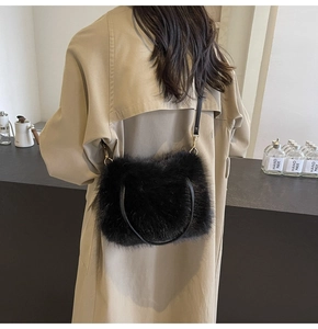 Detail shot of black plush faux fur crossbody bag with thin strap on a beige trench coat