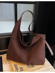 Brown faux suede hobo bag with adjustable shoulder strap leaning on books