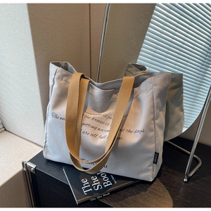 Detail of light grey canvas tote bag with brown handles and elegant script typography