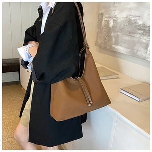 Detail of a brown matte leather shoulder bag with knotted strap and metal ball drawstring