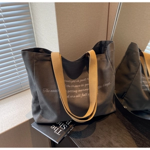 Detail of dark grey canvas tote bag with yellow straps and white text print
