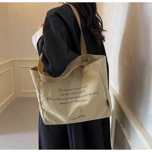 Detail view of a beige canvas tote bag with healing text and wide shoulder strap
