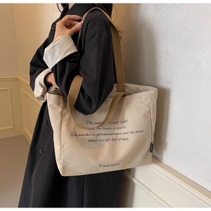 Detail of minimalist beige canvas tote bag with brown woven handles and typographic design