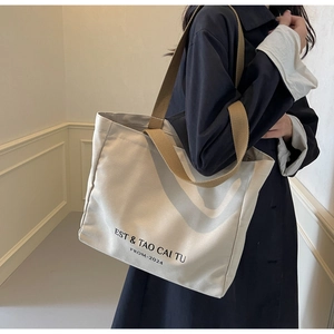 Detailed view of canvas tote bag featuring black lettering and brown wide web handles