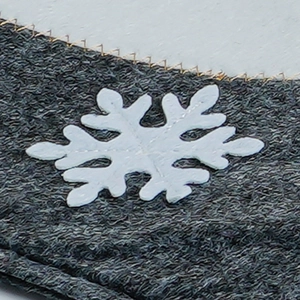 Detail of grey knitted toilet cover showing white snowflake pattern and gold stitching