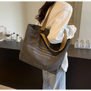 Detail of dark grey canvas tote bag featuring brown wide shoulder strap and artistic text