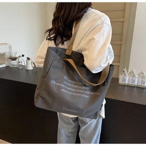 Grey canvas tote bag with brown straps shown on a model in a cozy coffee shop setting