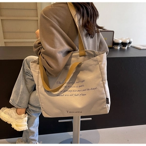 Canvas tote bag with khaki straps and motivational text shown in a cozy cafe setting