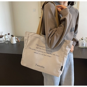 Detail of beige canvas tote bag with woven strap and text print in a cozy cafe setting