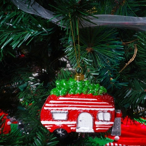 Rode vintage camper kersthanger met kerstboom hangend aan een feestelijke kerstboom