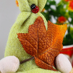 Macro detail of harvest gnome with green felt body, orange maple leaf and ladybug button