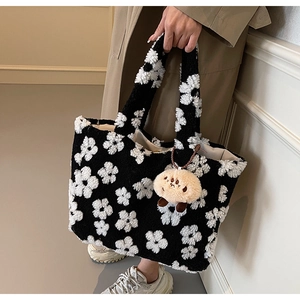 Detail of plush floral tote bag featuring black base with white flowers and cute bear charm