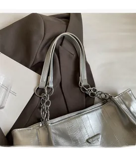 Detail of silver metallic tote bag featuring vertical embossing and triangular logo plaque