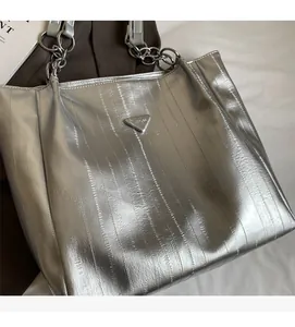 Detail of silver metallic tote bag with chain strap and triangular logo plaque
