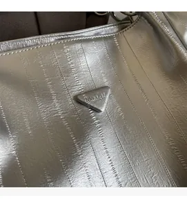 Close-up of textured silver tote bag featuring a triangular metallic logo plaque