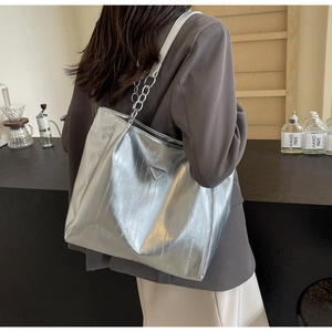 Detail of silver embossed tote bag featuring a metal triangle logo and chain strap