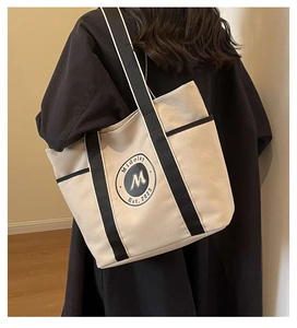 Detalle de un bolso tote de lona beige con correas negras y logo vintage sobre un modelo