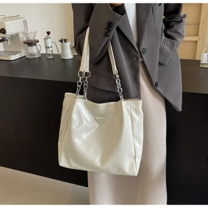 Detail of cream shoulder bag featuring textured finish and metal chain strap accent