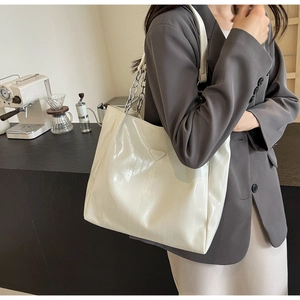 Close-up of a white tote bag featuring glossy patent leather texture and a metal chain strap