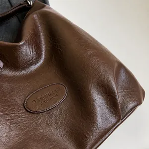 Detail of soft pebble grain leather and embossed logo on dark brown hobo shoulder bag