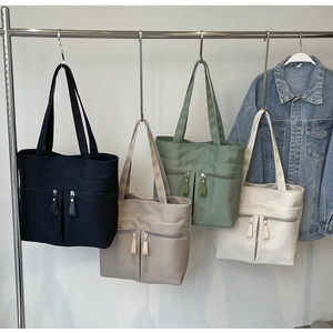 Dettaglio di quattro borse tote in tela nero, beige, verde e crema con doppie tasche a zip