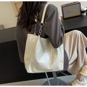 Close-up of white patent leather tote bag with silver chain strap and triangle logo plate