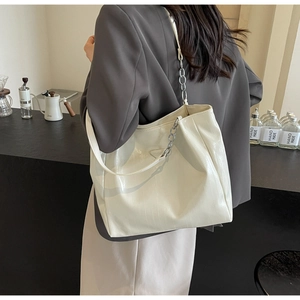 Detail of white glossy patent leather tote bag with silver chain and metal logo