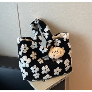 Close-up of black and white floral plush tote bag with a beige round charm on a magazine