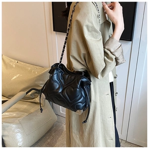 Detail of black quilted bucket bag featuring heart stitching and chain strap