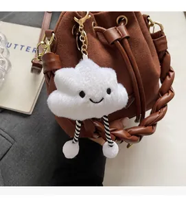 Detail of a brown suede bucket bag with woven handle and cute cloud plush charm
