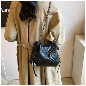 Detail of heart-quilted black shoulder bag with silver metal corners on beige trench coat