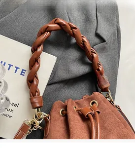 Detail of woven brown leather handle on a suede bucket bag with gold hardware